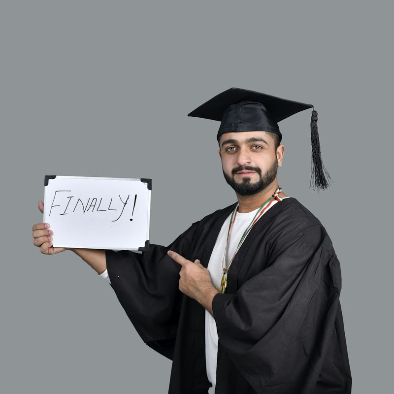 Smiling graduate in cap and gown holding a sign that reads “Finally!”